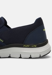 Marinblå sneaker med nät- och syntetöverdel, svart och vit sula, "FLEX-LITE"-märkning i neon-gult, och vadderad design för komfort.