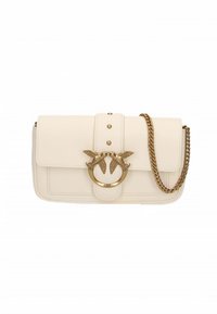 Kremet skinnveske med klaffelukking, gullfarget kjedestropp og dekorative fugle detaljer på et sirkulært metallstykke.