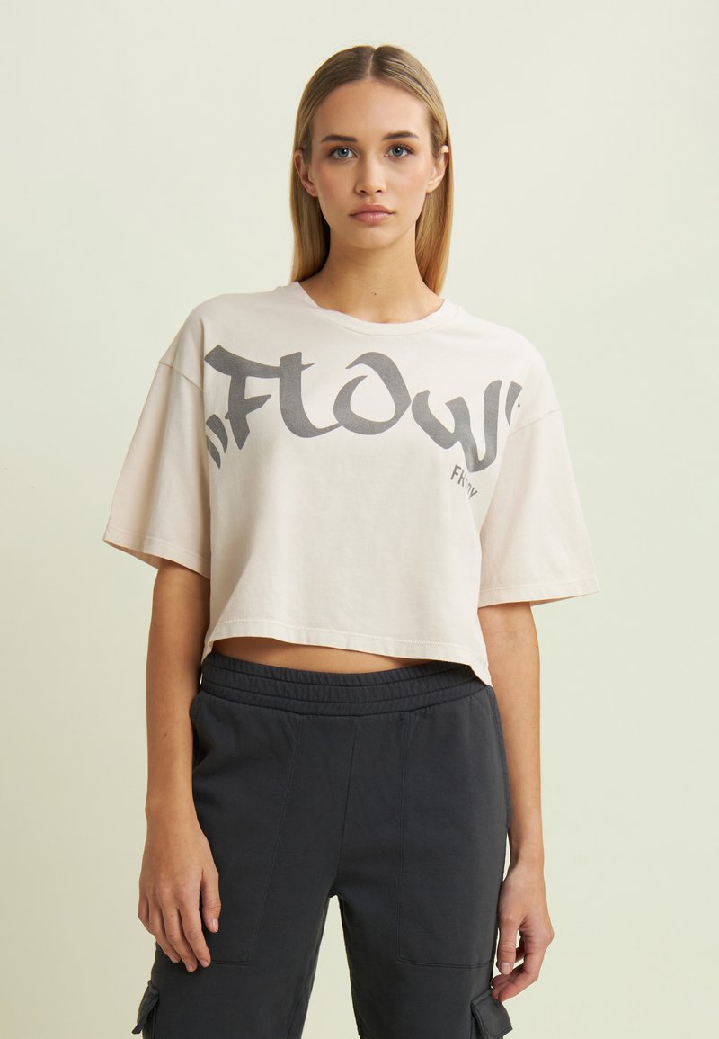 Camiseta cortada de color beige claro, hecha de algodón, con letras en negrita de color gris. Combinada con pantalones cargo oscuros de cintura elástica y con bolsillos.