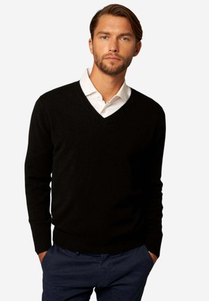 Schwarzer V-Ausschnitt-Pullover aus weichem Strickmaterial, mit langen Ärmeln und gerippten Bündchen, über einem weißen Hemd mit Kragen getragen.