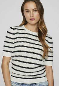 Suéter de punto con mangas cortas en blanco y negro a rayas, con un patrón texturizado y un cuello y dobladillo acanalados.