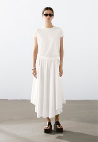 Hvid T-shirt med rund hals, parret med en lang hvid nederdel med elastisk talje. Sorte platform sandaler fuldender outfittet.