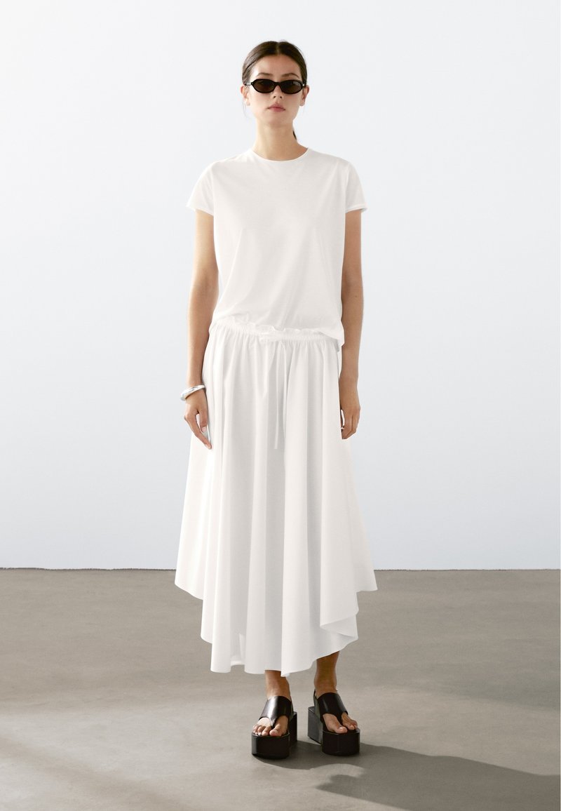 Hvid T-shirt med rund hals, parret med en lang hvid nederdel med elastisk talje. Sorte platform sandaler fuldender outfittet.