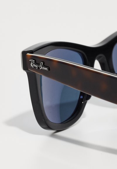 Уголемено изображение на черни и черупчести слънчеви очила Ray-Ban с сини огледални лещи на бял фон.