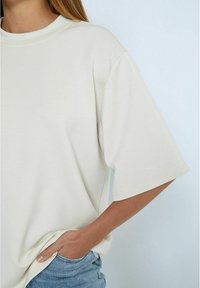 Camiseta corta de manga corta en color crema con un ajuste relajado, cuello redondo y tela suave, combinada con shorts de mezclilla azul claro.