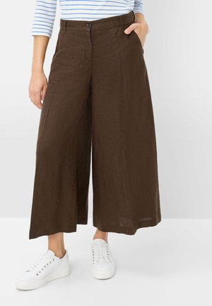 Bruine linnen wijde broek met een hoge taille, vooraan knoopsluiting en zijzakken, gecombineerd met witte sneakers. Soepele textuur.