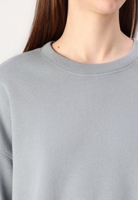 Ljust grå sweatshirt med rund hals, texturerad tyg och ribbade cuffs. Har en slät, mjuk yta.