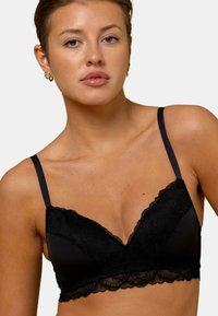 Bralette en dentelle noire avec un décolleté plongeant, des bretelles ajustables, un tissu doux et des accents en dentelle florale le long du bas et des bords.