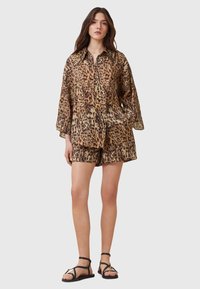Leopard print short-sleeve button-up shirt and matching shorts, made of lightweight fabric. Features a relaxed fit and black sandals.