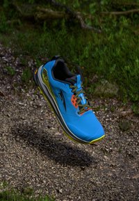 Chaussure de course bleue avec des accents gris et jaunes, tige texturée, intérieur noir et lacets multicolores, présentée en l'air sur fond naturel.