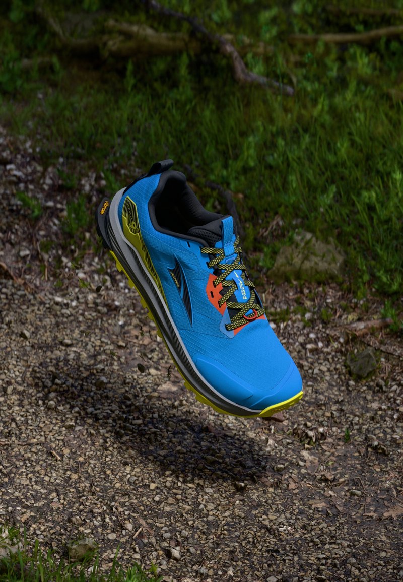 Chaussure de course bleue avec des accents gris et jaunes, tige texturée, intérieur noir et lacets multicolores, présentée en l'air sur fond naturel.