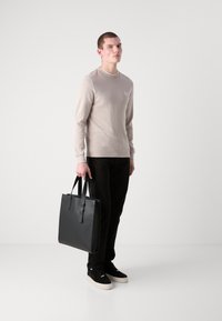 Beige langermet skjorte med ribbet tekstur, svart tote bag, svarte bukser og svarte sneakers med en tykk hvit såle. Enkle designelementer.