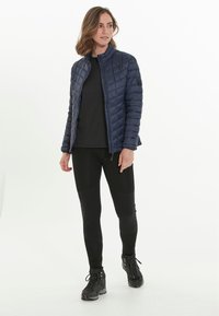 Veste matelassée navy avec col montant, fermeture éclair, assortie à un haut noir et un legging noir. Portée avec des bottes de randonnée noires avec lacets.