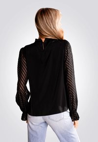 T-shirt noir avec de longues manches transparentes rayées, col haut et détail de clé à l'arrière. Tissu léger avec une texture lisse. Coupe décontractée.