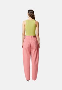Top verde senza maniche e jeans larghi fucsia a vita alta. Il tessuto appare liscio; i jeans presentano tasche posteriori e una patch in pelle.