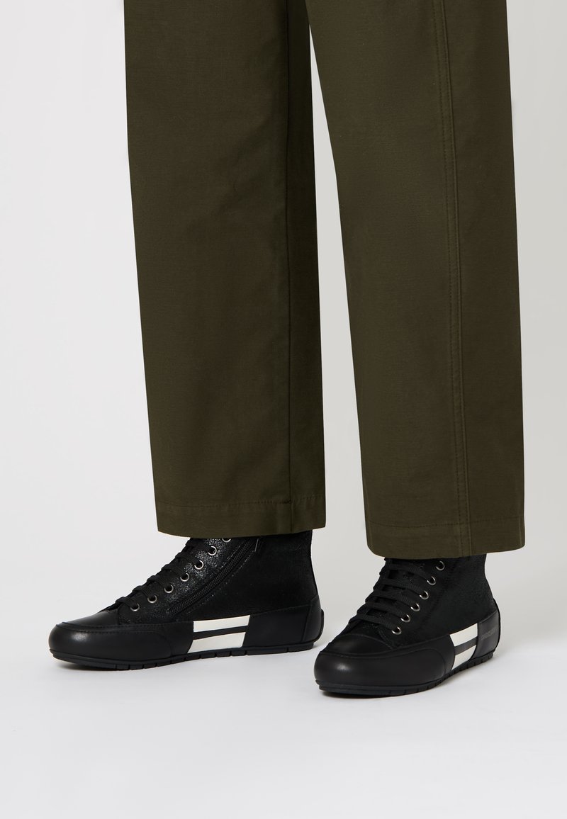 Sneakers alte nere con tessuto a trama e finitura in pelle, con strisce orizzontali bianche, abbinate a pantaloni verde oliva.