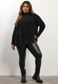 Czarny sweter w prążki z koronkowym dołem, zestawiony z błyszczącymi czarnymi legginsami i botkami na kostkę. Ubiór charakteryzuje się luźnym krojem i teksturowanymi detalami.