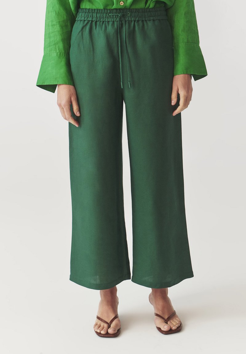 Groene linnen wijdvallende broek met een trekkoord in de taille, met een soepele textuur en een ontspannen pasvorm, gecombineerd met simpele platte sandalen.
