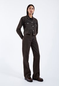 Dunkelblaue Jeansjacke mit cropped Design und zwei Brusttaschen, kombiniert mit hochgeschnittenen, weit geschnittenen dunklen Jeans und klobigen schwarzen Plateauschuhen.