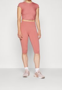 Sportowy zestaw w odcieniu przybrudzonego różu, składający się z dopasowanego topu na krótki rękaw oraz legginsów o długości midi, wykonany z elastycznego materiału. Połączony z jasnoróżowymi trampkami.