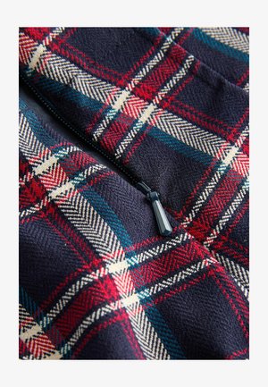 Artimas jūros mėlynumo audinio vaizdas su raudonos, baltos ir žalios spalvų languoto rašto, centre esanti juoda užtrauktuko traukimo detalė.