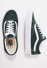 Grüne Wildlederschuhe mit weißen Akzenten, klassisches Low-Top-Design, flache weiße Gummisohle und Schnürverschluss. Vans-Logo innen sichtbar.