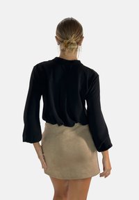 Zwart longsleeve top met een relaxte pasvorm en subtiele textuur, gecombineerd met een korte tan suède rok. Minimalistisch ontwerp zonder zichtbare patronen.