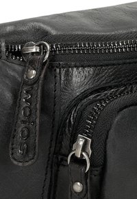 Borsa in pelle nera con finitura testurizzata, dotata di hardware in argento, due zip e un'etichetta con logo. Primo piano dei dettagli della zip.
