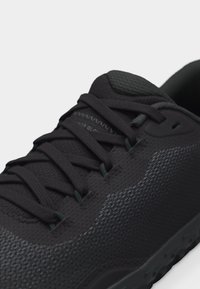 Κοντινή λήψη ενός μαύρου αθλητικού παπουτσιού με υφή στο πάνω μέρος, μαύρα κορδόνια και μαξιλαρωμένη γλώσσα σε λευκό φόντο.