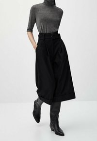 Zwarte hoog- taille culottes met een riem, gecombineerd met een aansluitende grijze coltrui. De outfit heeft een gestructureerde stof en kniehoog zwarte laarzen.