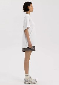 Witte oversized t-shirt met korte mouwen, gecombineerd met grijze shorts met tekst en grijs-zilveren sportschoenen. Eenvoudig ontwerp, relaxte pasvorm.