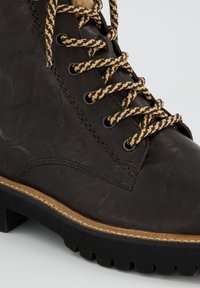 Bota de senderismo de cuero marrón con cordones en contraste beige y marrón, superficie texturizada, suela negra resistente y detalles de costura a lo largo de la suela.