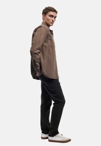 Bruine lange mouwen shirt met een zak aan de voorkant, gecombineerd met zwarte broek en witte sneakers. Het shirt heeft een relaxte pasvorm en een gladde stoftextuur.
