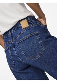 Blå denimjeans med hög midja, med en läderetikett på baksidan, tonala sömmar och klassisk femficksdesign.