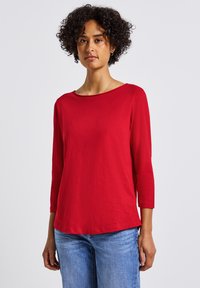 Rotes langärmliges T-Shirt mit einem Bootsausschnitt, aus einem weichen, leichten Material. Hat eine lockere Passform und überlappende Seitennähte.