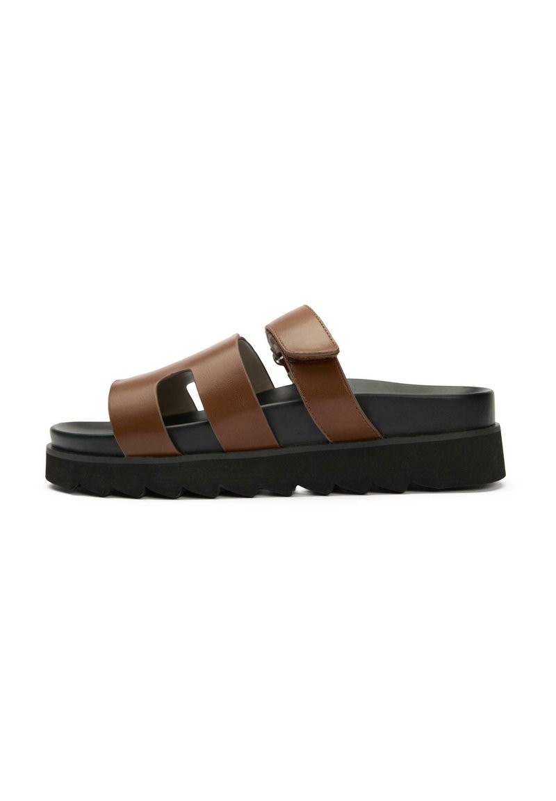 Brown leather sandals with two wide straps, adjustable buckle, and a thick black rubber sole featuring a zigzag pattern.