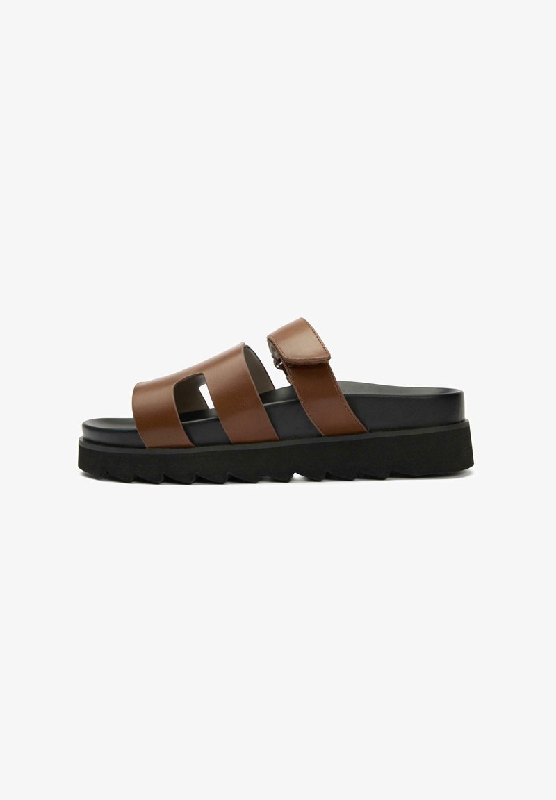 Brown leather sandals with two wide straps, adjustable buckle, and a thick black rubber sole featuring a zigzag pattern.