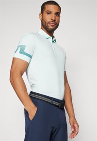 Hellblaues Poloshirt mit einem dezenten gestreiften Design an den Ärmeln, kombiniert mit navyblauen Hosen und einem strukturierten schwarzen Gürtel mit silbernen Akzenten.