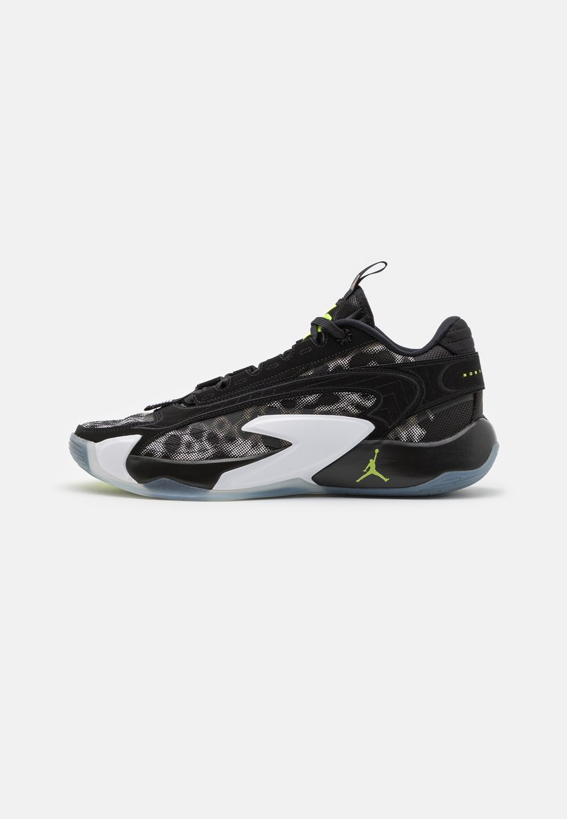 Zapatillas deportivas negras con parte superior de malla, acentos brillantes y una entresuela blanca. Presentan detalles en verde brillante y una suela translúcida.