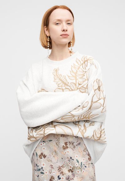 Φούτερ σε ανοιχτό γκρι βαμβάκι με έντονη μπεζ κεντήματα λουλουδιών, με φαρδιά μανίκια και άνετη εφαρμογή, σε συνδυασμό με φούστα με λουλουδάτο μοτίβο.