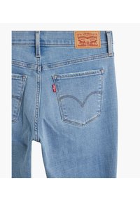 Jeans de denim azul claro con una etiqueta de cuero marrón en la cintura, dos bolsillos traseros con costuras arcuadas y una pequeña etiqueta de tela roja con la marca.