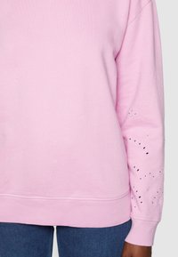 Sudadera rosa de corte relajado, con puños acanalados y elaborados detalles de ojal en la manga. Fabricada en suave tela de algodón.
