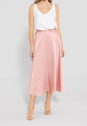 Light pink satin midi skirt with a smooth texture and a flowy design, paired with a white sleeveless top. Silvery strappy sandals complete the look.