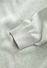 Manga de suéter de punto gris claro con puño acanalado apoyada sobre un fondo de tela a juego.