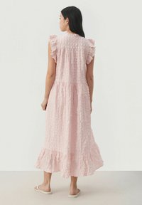 Rosa klänning som når knäna, med texturerad tyg, volangärmar och en flerlagers nederdel. Slätt material med en lätt och luftig design.