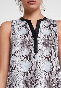 Bezramkowy top z wzorem w węże w kolorze białym i brązowym z czarnym satynowym wykończeniem przy dekolcie. Gładka tekstura.