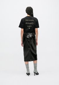 Juoda marškinėliai su auksiniais užrašais, derinami su blizgia juoda pieštuko formos sijonu. Pilkos iki kelių aukštos kojinės ir juodi aukštakulniai batai užbaigia aprangą.