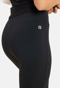 Leggings sportivi neri con un tessuto liscio e elasticizzato, vita alta e un piccolo logo vicino anche all'anca destra.