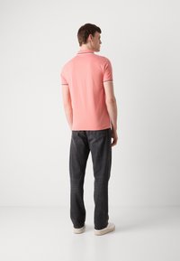 Polo rose clair à coupe slim, avec un col et des finitions de manches en marine contrastant. Associé à un jean foncé et des baskets blanches.