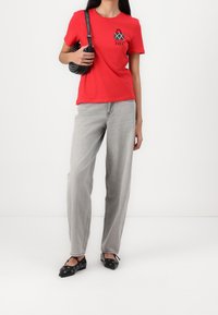 Camiseta de algodón roja con mangas cortas y un estampado gráfico, combinada con jeans de tiro alto grises y zapatos planos negros con detalles de ojales.